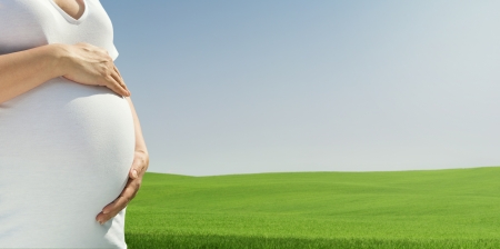 Close up of pregnant woman relaxing at the empty sunny field with copy spaceの写真素材