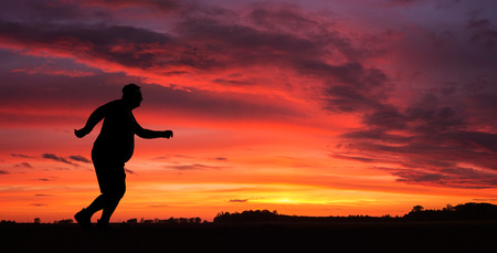 Silhouette of funny overweight man jogging at the sunsetの写真素材
