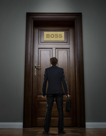 Small young businessman standing in front of the boss office doorの写真素材