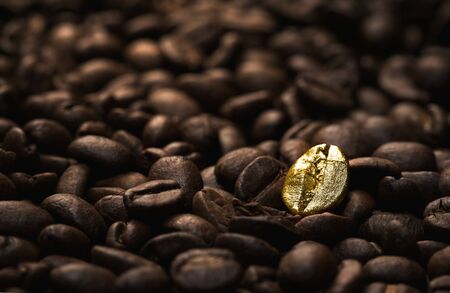 Individuality, standing out  from a crowd concept, close up of a single bright, gold coffee bean over many dark ones with copy spaceの写真素材