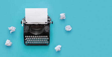 Vintage typewriter and crumpled paper over blue background with copy spaceの写真素材