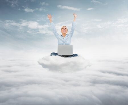 Reach the sky concept. Young succesful  businesswoman with laptop sitting on the cloud high up in the skyの写真素材