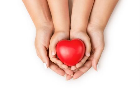 Love, family concept. Close up of mother and children hands holding red rubber heart together isolated on white backgroundの写真素材