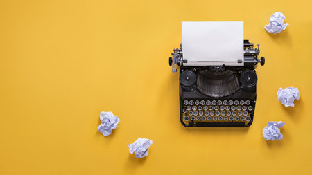 Vintage typewriter and crumpled papers over yellow background with copy spaceの写真素材