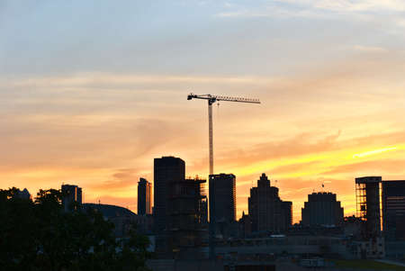 A skyline view of a city with a lifting crane in a construction site in the middle at sunsetの写真素材