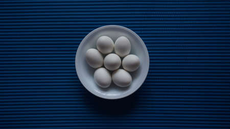 White eggs in a white dish with a blue texture backgroundの写真素材