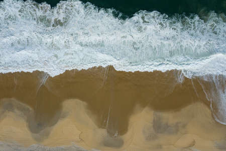 Wave and sand. Top view of a beach with bare footprints along.