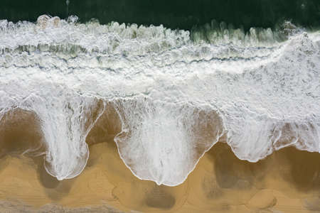 Wave and sand. Top view of a beach with bare footprints along.