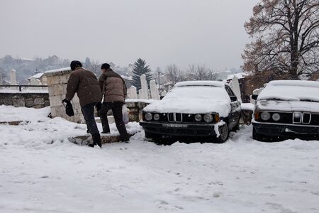 Sarajevo, Bosnia and Herzegovina - December 16, 2016: Two men heading towards cemetery during a snowfall this noon in Sarajevo.のeditorial素材