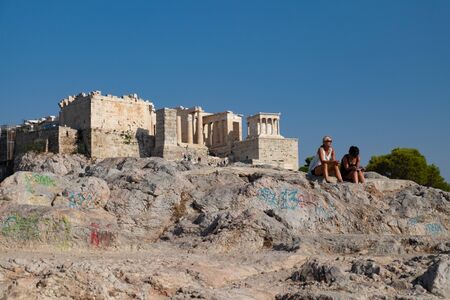 Athens, Greece - August 17, 2016: Unknown female tourists sits relaxing on the rock in front of the Parthenon temple.のeditorial素材