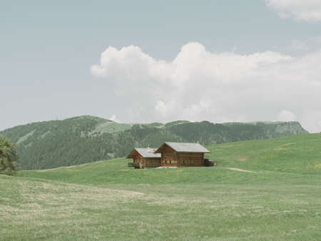 Wooden house on a meadow with mountains in the background.