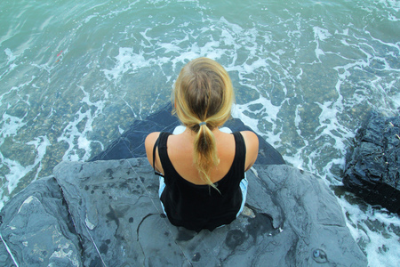Outdoor woman alone sitting on stone coast and looking at seaの写真素材