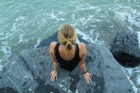Outdoor woman alone sitting on stone coast and looking at seaの写真素材