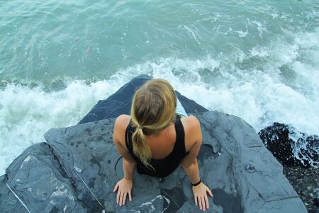 Outdoor woman alone sitting on stone coast and looking at seaの写真素材