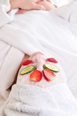 A woman at the spa with a facial mask, cucumber and strawberriesの写真素材
