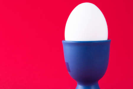 A white egg in a blue egg cup with a red backgroundの写真素材