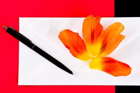 Petals, pen and an envelope on a red backgroundの写真素材