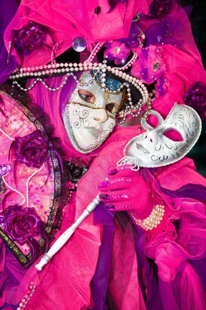 Person holding a silver mask wearing a pink costume at the Venice Carnivalの写真素材