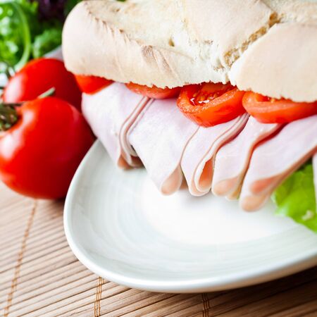 A large ham and tomato baguette on a plateの写真素材