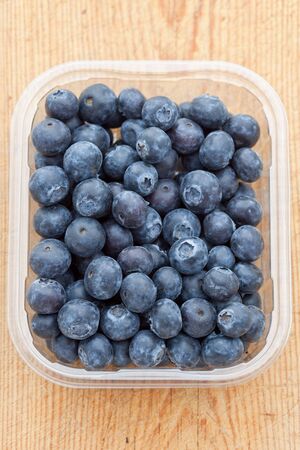 Delicious fresh blueberries in a plastic container on a wooden board