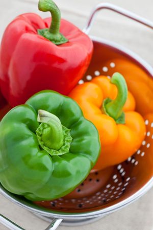 Red, green and orange bell peppers in a silver colanderの写真素材