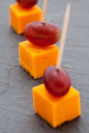 Party snacks. Cheese cubes and grapes on a slateの写真素材