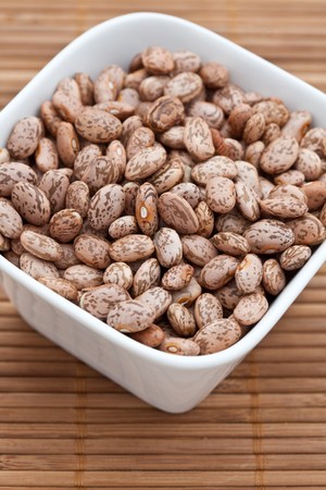 Dried pinto beans in a white bowl on a bamboo matの写真素材