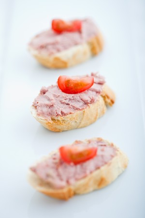 Three baguette slices with liver and apple pate and a thin tomato slice on top. Shallow DOFの写真素材