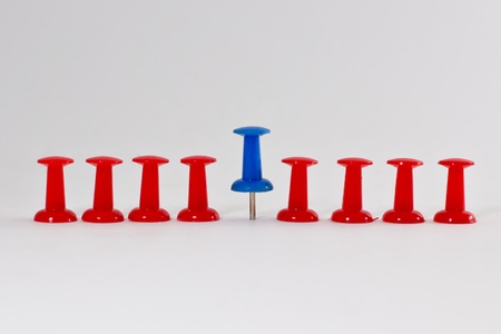 row of red pins with a blue pin in middle isolated on white backgroundの写真素材