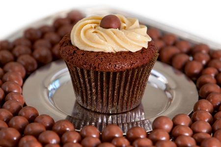 Chocolate malt cupcake surrounded by malt balls on steel plate.の写真素材