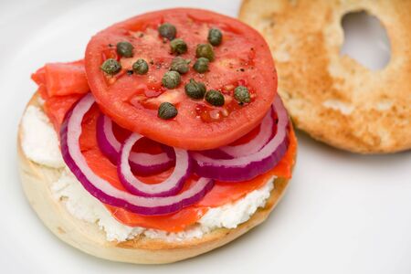 Bagel on a plate with smoked salmon, cream cheese, tomato, onion, and capers.の写真素材