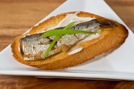 Single sardine on a slice of toasted baguette garnished with green onion on white plate.の写真素材