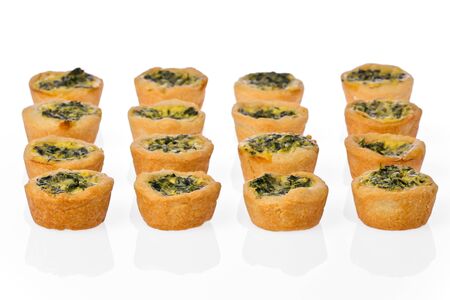 Several homemade mini spinach quiche in rows on a white background.の写真素材