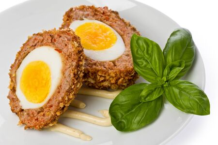 Two halves of a scotch egg on a white plate with mustard sauce.