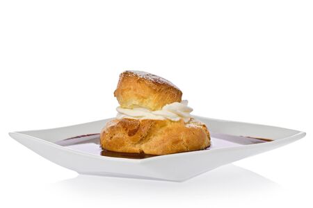 Cream puff with raspberry filling in a chocolate sauce on a square dessert plate.の写真素材