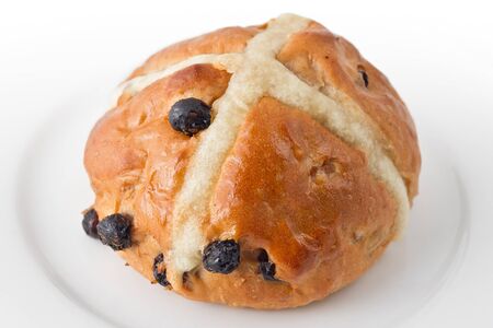 Traditional hot cross bun on white plate.