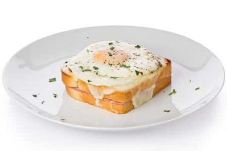 A ham and cheesed sandwich with bechamel sauce and topped with a fried egg, known as Croque-madame, on a white plate against a white background.の写真素材