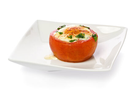 A single baked tomato stuffed with an egg, on a white plate against a white background.の写真素材