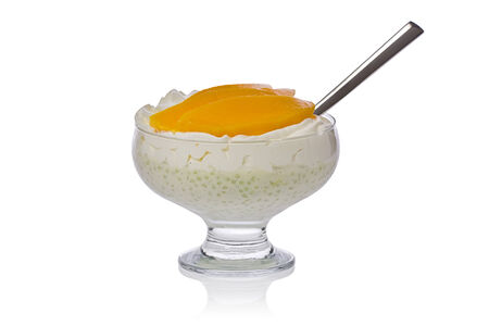 Tapioca pudding with whipped cream, slices of mango, and a spoon,  in a glass bowl against a white background.の写真素材