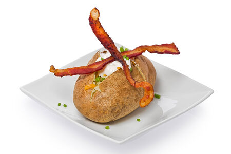 Baked potato with two thin strips of bacon, cheese, sour cream and  garnished with green onion against a white background.の写真素材