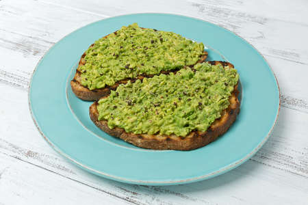Two slices of avocado toast with cracked black pepper on a blue plate.の写真素材