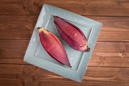 Two Banana blossoms, or banana hearts, on a small square plate on a wood background.の写真素材