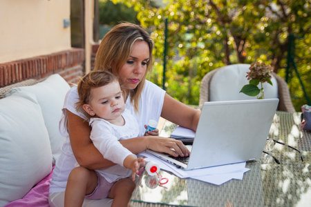 Mother with her baby in her arms teleworking in her garden at homeの写真素材
