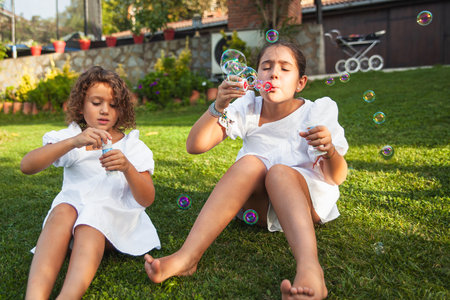 Two sister girls entertained playing with the soap bubbles in the garden