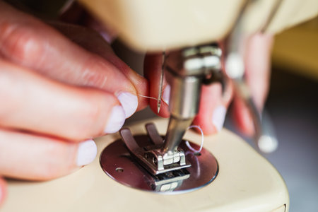 Detail of the hands of a dressmaker threading the needle of the machine