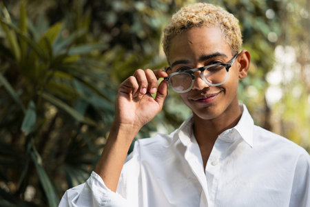 Portrait of young black man with blond hair with prescription glasses in greenhouseの写真素材