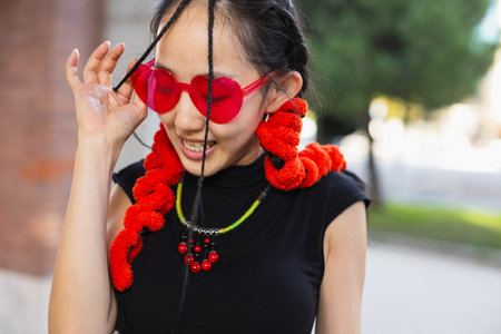"A candid shot of a female street dancer smiling while adjusting her heart-shaped red sunglasses, adorned with vibrant red accessories.の写真素材
