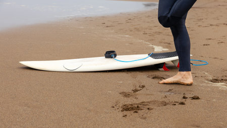 Cut out of a surfer's legs on the beach with a surfboard.