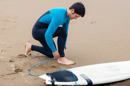 Young surfer on the shore tying his surfboard to his ankle to enter the sea to surf