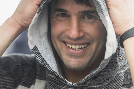 A smiling surfer wrapped in a towel enjoys the warm comfort after a satisfying surf session,...